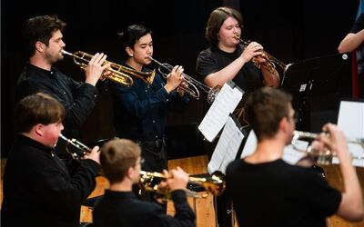 Sechs Trompeterinnen und Trompeter stehen im Halbkreis auf der Bühne und Musizieren gemeinsam.