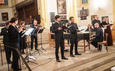 In der Stiftskirche Herrenberg musiziert ein Ensemble aus Flöten, Streichern, Orgel, Cembalo und Sängern. Die Instrumentalisten bilden einen Halbkreis um die vier Sänger und das Cembalo.