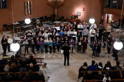 Eine Gruppe von Kindern spielt Blockflöten in einem Kirchenkonzert, dirigiert von einer Person, während das Publikum zuschaut.